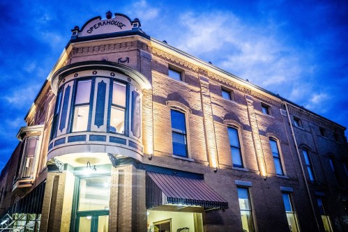 Historic opera house building illuminated at dusk, showcasing architectural details and a welcoming entrance.