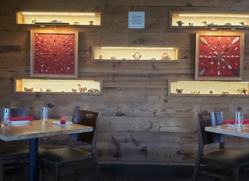 Cozy restaurant interior with wooden walls, illuminated shelves displaying art, and two empty tables set for dining.