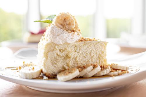 A slice of banana cheesecake topped with whipped cream and banana slices, garnished with mint leaves.