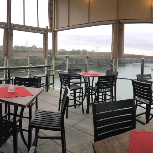 A riverside restaurant with empty tables and chairs, featuring a scenic view through large windows.