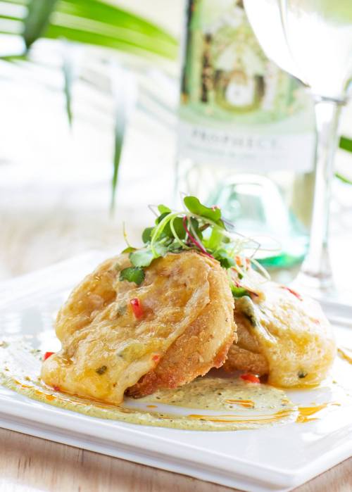 A plate of crispy fried food topped with herbs and sauce, with a bottle of wine and a glass in the background.