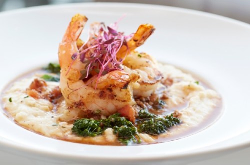 A plate of creamy risotto topped with grilled shrimp, garnished with microgreens and a drizzle of sauce.