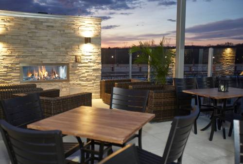 A cozy outdoor seating area with a stone fireplace, wooden tables, and a sunset backdrop.