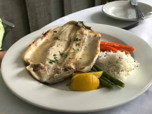 A plate featuring grilled fish, rice, carrots, green beans, and a lemon wedge, served on a white tablecloth.