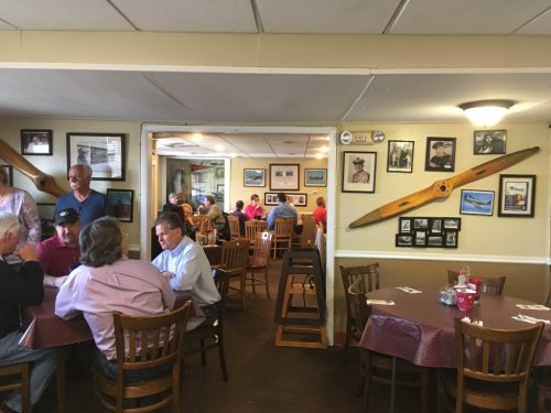 A cozy restaurant interior with wooden tables, patrons dining, and walls adorned with photos and airplane propellers.