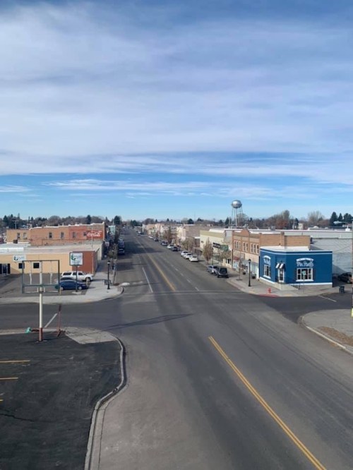 A wide view of a small town street lined with buildings, under a clear blue sky with a few clouds.