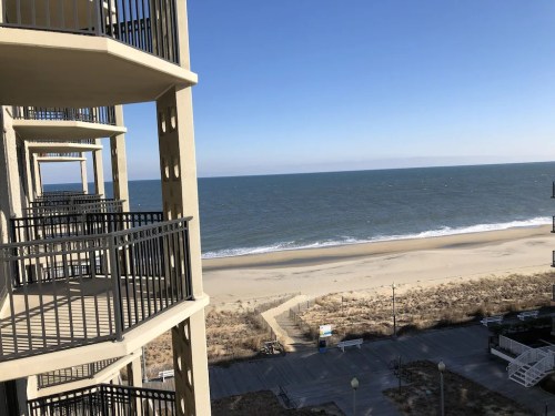 View from a balcony overlooking a sandy beach and calm ocean under a clear blue sky.