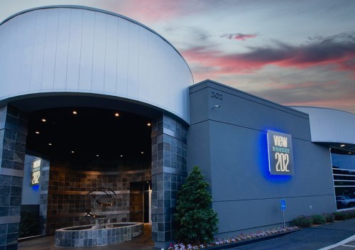Modern building entrance with a large illuminated sign reading "202" against a colorful sunset sky.