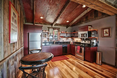 Cozy kitchen with wooden beams, dark cabinets, stainless steel appliances, and a round table on hardwood floors.