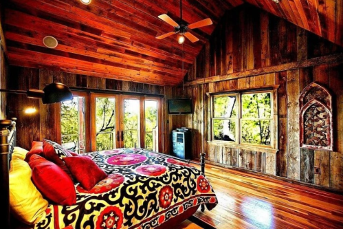 Cozy bedroom with wooden walls, a patterned bedspread, and large windows overlooking greenery.