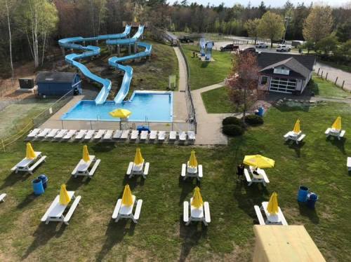 Aerial view of a water park featuring a pool, water slides, and lounge chairs with yellow umbrellas on a grassy area.