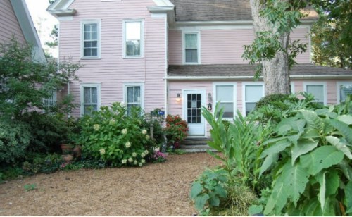 A charming pink house surrounded by lush greenery and colorful flowers in a garden setting.