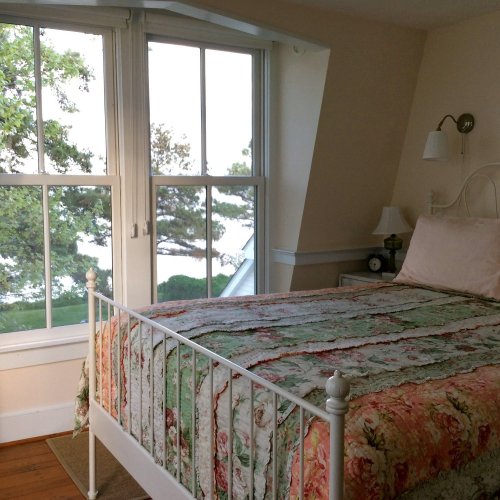 Cozy bedroom with a floral quilt, white bed frame, and large windows overlooking a serene outdoor view.