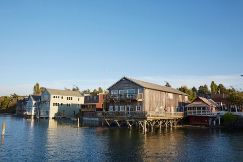 A scenic view of colorful waterfront buildings on stilts, reflecting in calm water under a clear blue sky.