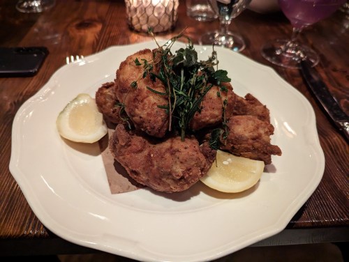 A plate of crispy fried chicken pieces garnished with herbs and served with lemon wedges.