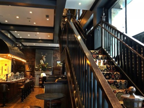Interior of a stylish restaurant featuring a staircase, bar area, and decorative elements on the walls.