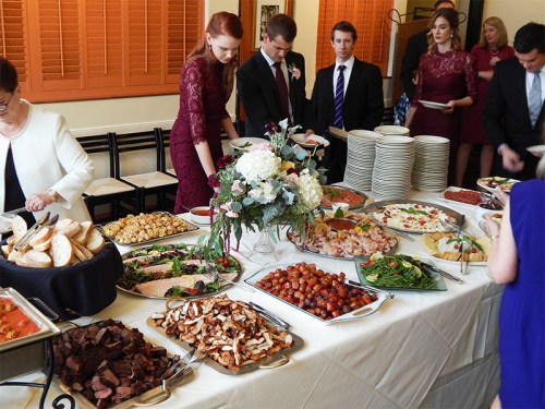 A buffet table filled with various dishes, as guests in formal attire serve themselves at a gathering.