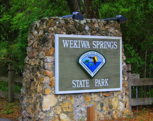 Sign for Wekiwa Springs State Park, featuring a stone structure and lush greenery in the background.