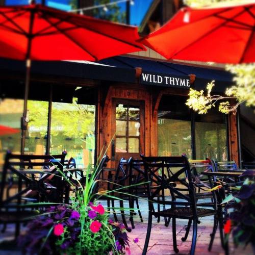 Outdoor seating area of a restaurant named "Wild Thyme," featuring red umbrellas and colorful flowers.