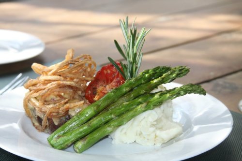 A plate of grilled asparagus, mashed potatoes, a roasted tomato, and crispy fried onions.