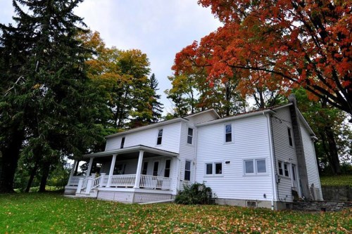 A white two-story house surrounded by trees with vibrant autumn leaves and a grassy yard.