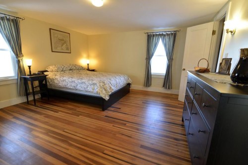 Cozy bedroom with a bed, nightstands, and a dresser, featuring hardwood floors and soft lighting.