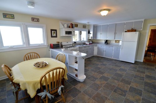 Bright kitchen with a round table, wooden chairs, and modern appliances, featuring light-colored cabinets and tiled floor.