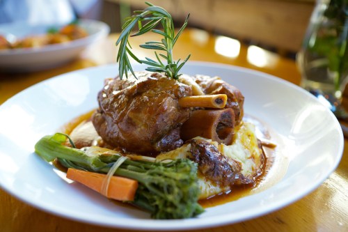 A plate of tender braised meat with a sprig of rosemary, served with mashed potatoes and vegetables.