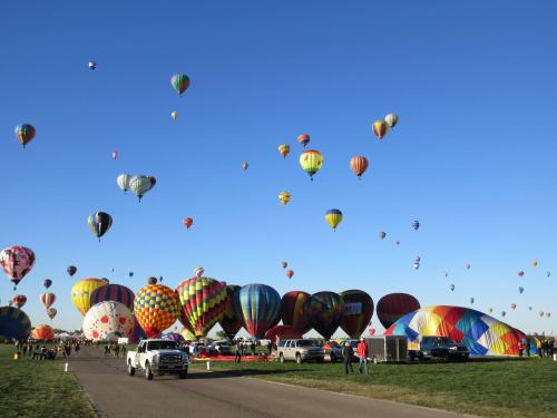 A vibrant scene of colorful hot air balloons in the sky, with people and vehicles on the ground below.