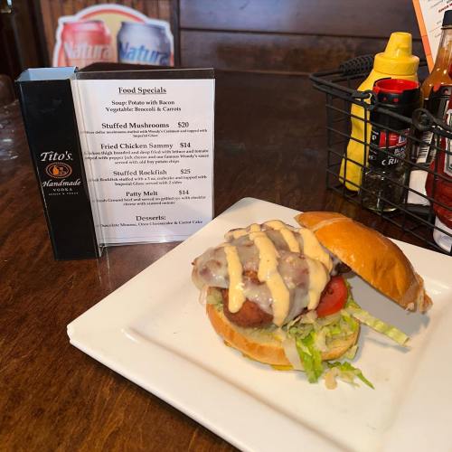 A close-up of a burger with a patty, lettuce, tomato, and sauce, alongside a menu and condiments on a table.