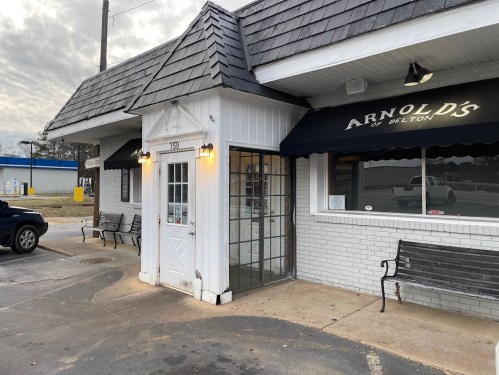Exterior view of Arnold's restaurant, featuring a white entrance, black awning, and benches outside.