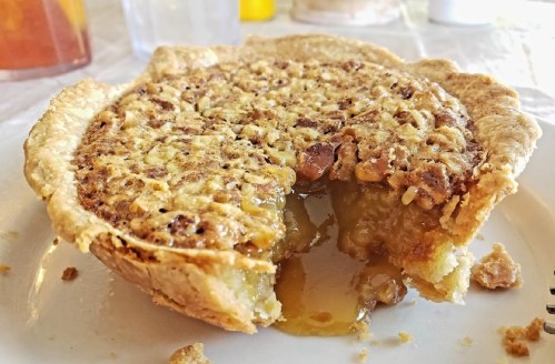 A slice of pie with a golden, gooey filling and a flaky crust, sitting on a white plate.