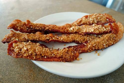 Crispy, golden-brown bacon strips coated in a crunchy, crumbly topping on a white plate.