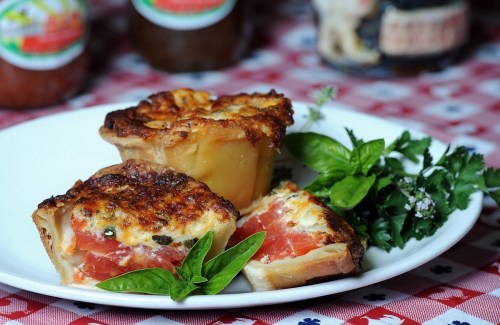A plate of baked tomato and cheese tartlets, garnished with fresh herbs on a checkered tablecloth.