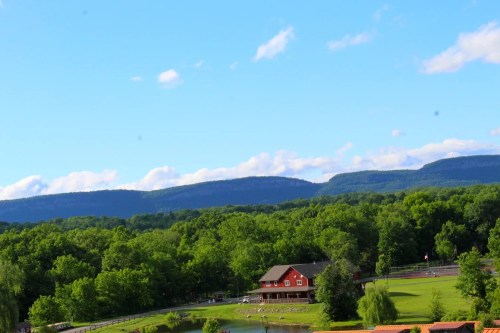 A red house surrounded by lush green trees, with mountains and a blue sky in the background.