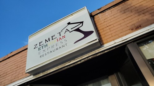 Sign for "Zemeta Ethiopian Express Restaurant" on a brick building against a blue sky.