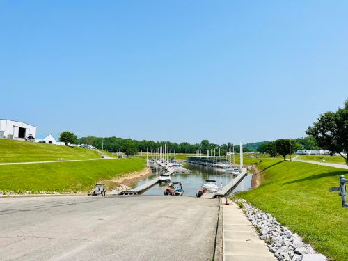 A serene marina with boats docked along a calm waterway, surrounded by green hills and a clear blue sky.
