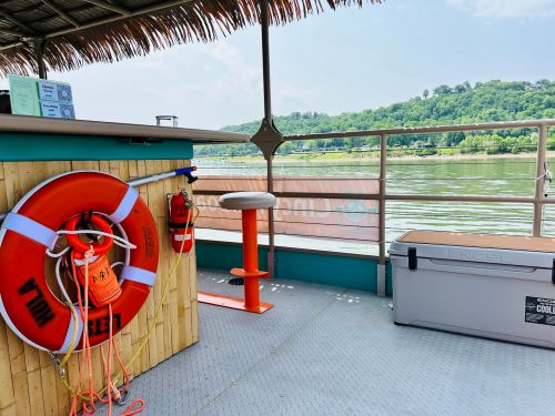 A boat deck featuring a life ring, a bar area, and a cooler, with a scenic view of green hills in the background.