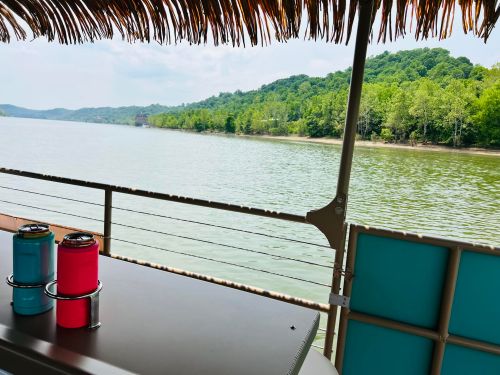 A view of a calm lake surrounded by green hills, with colorful drink containers on a table in the foreground.