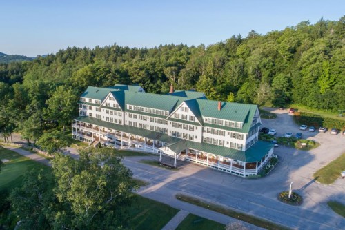 Aerial view of a large, green-roofed hotel surrounded by trees and a parking area.