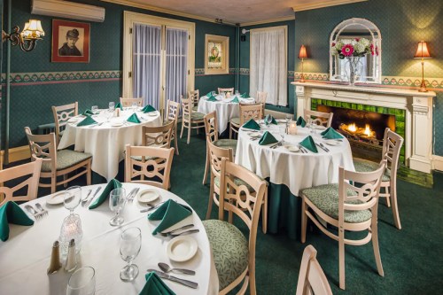 Elegant dining room with round tables set for a meal, featuring green accents and a cozy fireplace.