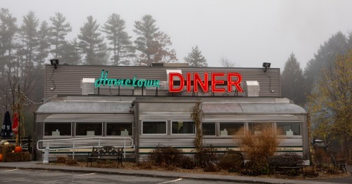 A foggy scene featuring a retro diner with a neon "Hometown Diner" sign and surrounding trees.