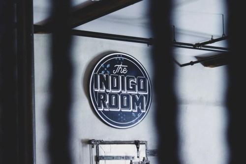Sign for "The Indigo Room" on a concrete wall, partially obscured by vertical bars.