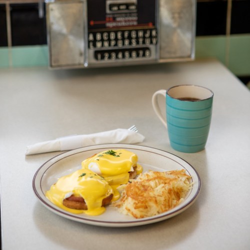 A plate of eggs Benedict with hollandaise sauce, hash browns, and a cup of coffee on a diner table.