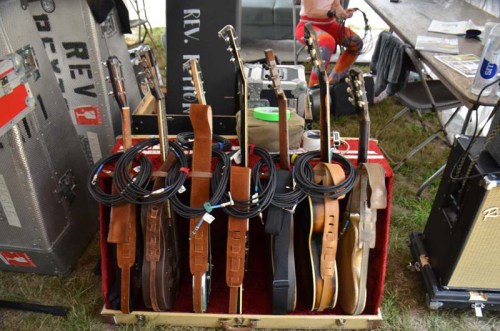 A collection of guitars and cables displayed on a red velvet-lined case at an outdoor event.