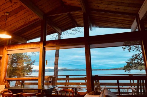 Cozy cabin interior with large windows showcasing a serene lake view and trees outside at dusk.