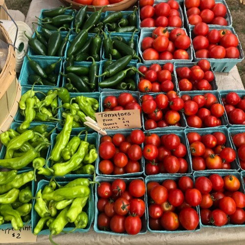 A colorful display of fresh vegetables, including green peppers and red tomatoes, in small containers at a market.