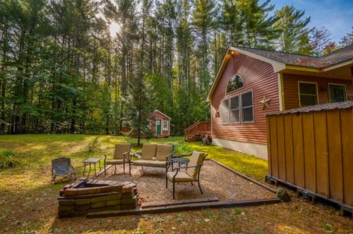 A cozy cabin surrounded by trees, featuring a fire pit and seating area in a serene outdoor setting.