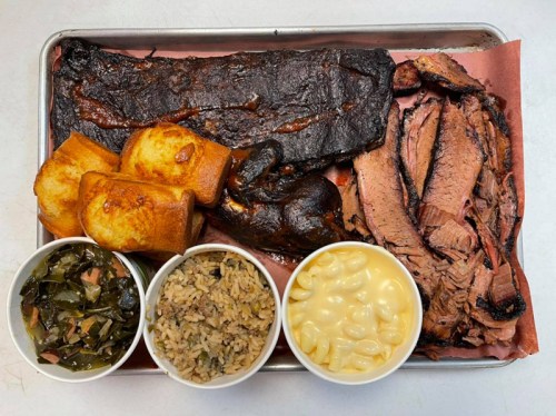 A tray of barbecue featuring brisket, ribs, cornbread, collard greens, rice, and macaroni and cheese.
