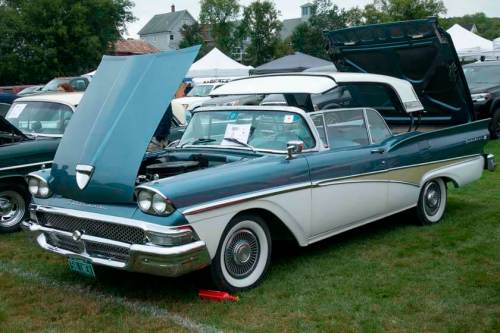 A classic two-tone convertible car with its hood open, parked on grass at a car show.